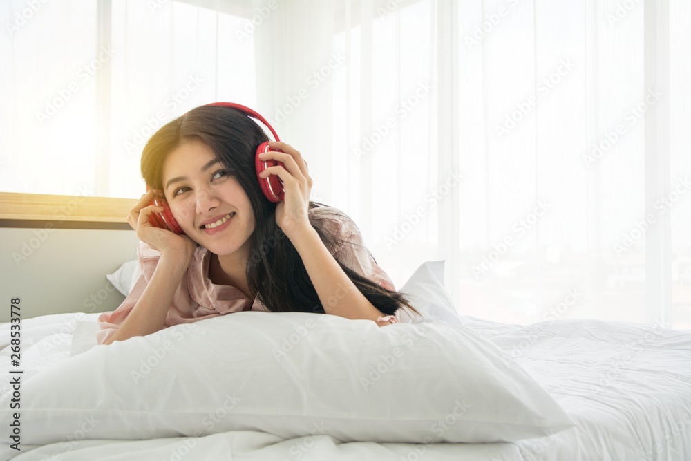 Portait of smiling lady in pink pajama wake up listening to music with headphone on the bed Portait of smiling lady in pink pajama wake up listening to music with headphone on the bed