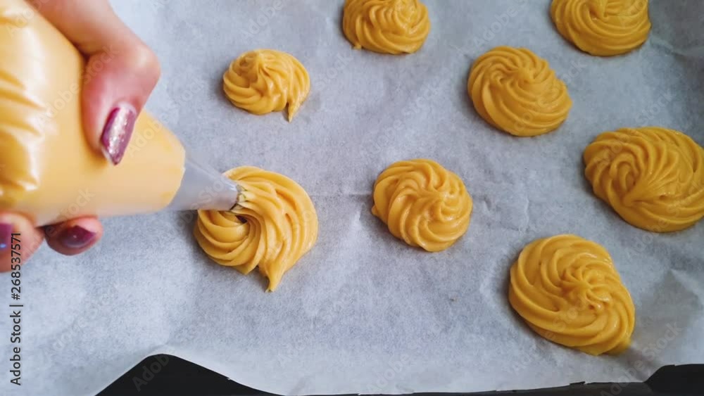 Female hands holding piping bag and making cream puffs in the kitchen at home. Female hands holding piping bag and making cream puffs in the kitchen at home.