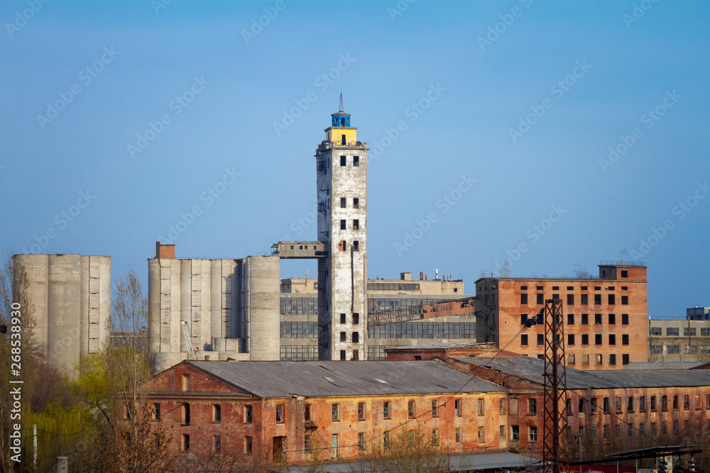 Abandoned damaged old granary against town and blue cloudy sky