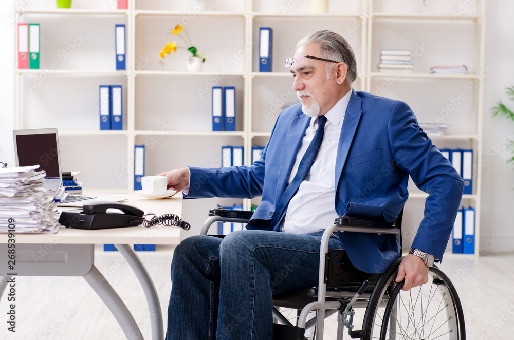 Aged employee in wheelchair working in the office Aged employee in wheelchair working in the office