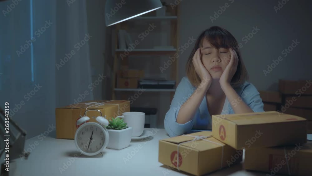 Young Asian entrepreneur business woman owner of SME sleepy exhausted working at office desk in night at home, feeling sick and tired. Small business owner at home office concept.