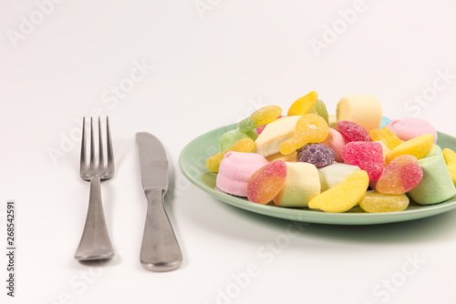 Fork, knife and plate with marshmallow and gummy candies isolated on white background.