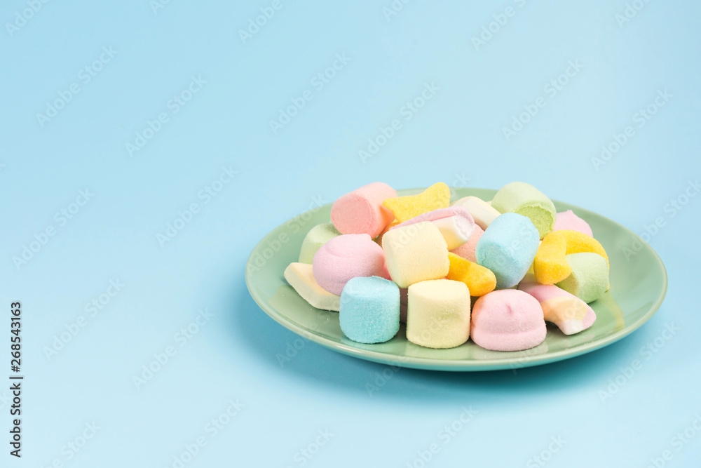 Green plate with marshmallow isolated on blue background. Green plate with marshmallow isolated on blue background.