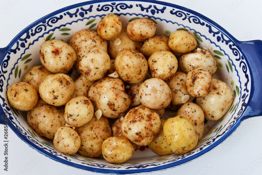 Young peeled potatoes in spices prepared for roasting in a ceramic form on a white background