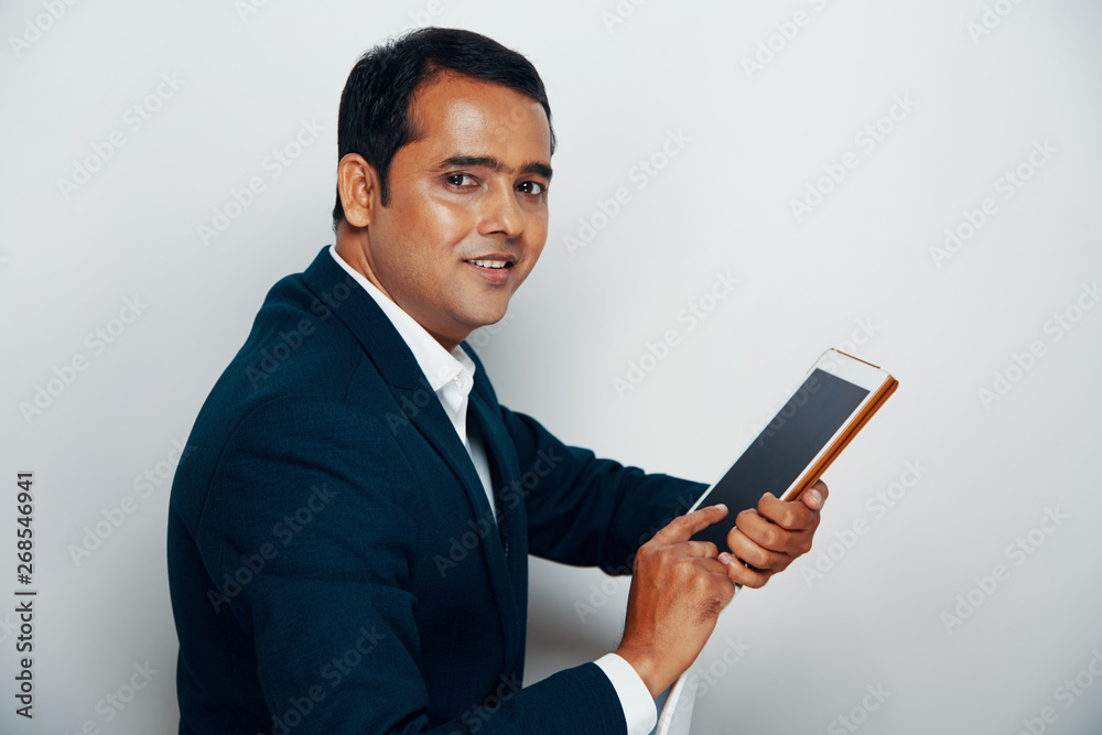 Portrait of Indian professional in suit working online on digital tablet and smiling at camera over white background Portrait of Indian professional in suit working online on digital tablet and smiling at camera over white background