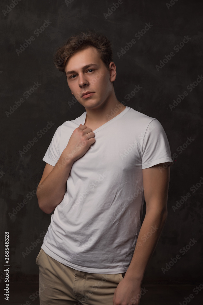 Handsome young man with a stylish haircut in a white shirt on black background looking at camera.