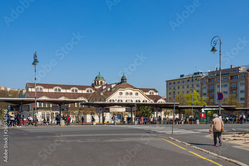 Outdoor sunny street view at bus station with people wait for buses, and background of Budova Městské tržnice, Municipal Market Building, against blue sky in Karlovy Vary, Czech Republic. photo