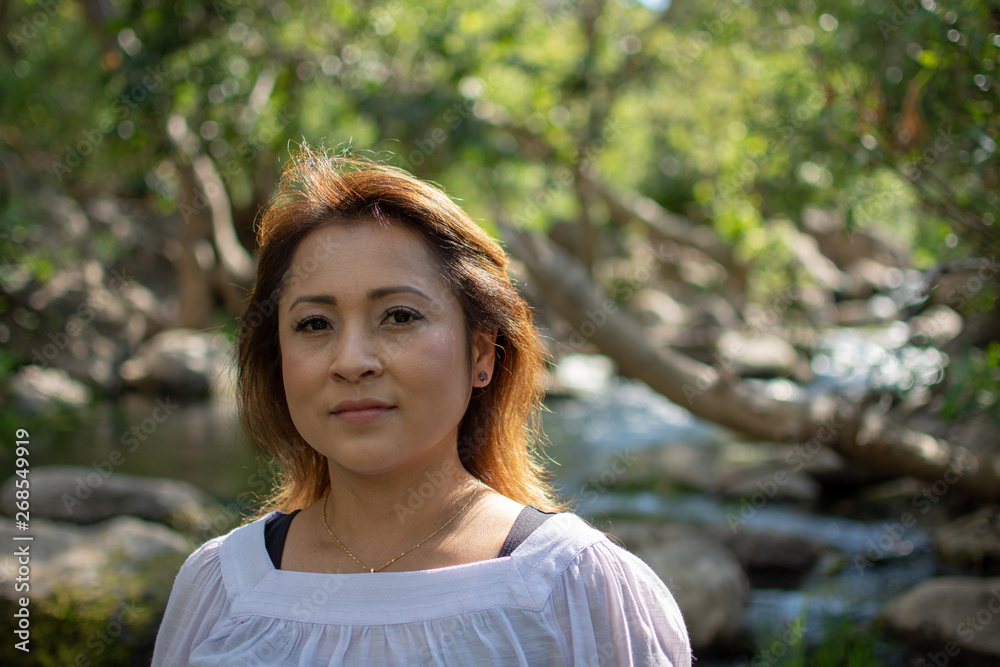 Latina woman with serious expression standing in the shade with glowing hair in a stream with waterfalls in the background Latina woman with serious expression standing in the shade with glowing hair in a stream with waterfalls in the background