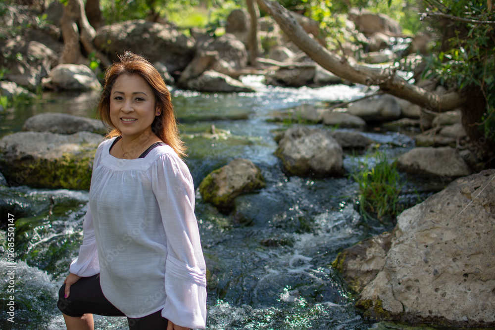 Latina woman with smile standing in the shade with glowing hair in a stream with waterfalls in the background Latina woman with smile standing in the shade with glowing hair in a stream with waterfalls in the background