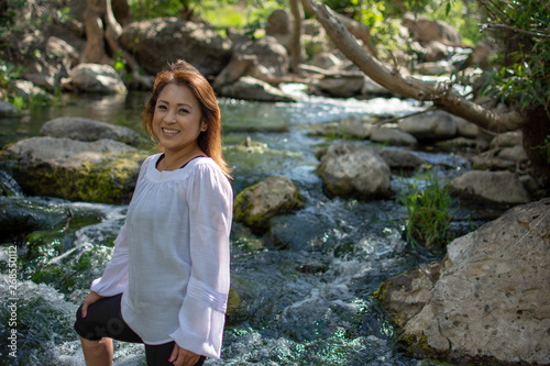 Latina woman with smile standing in the shade with glowing hair in a stream with waterfalls in the background