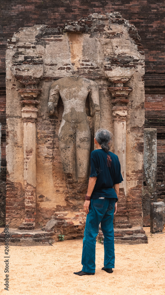 Senior asian traveller looking up to a buddha ruin in Sri Lanka