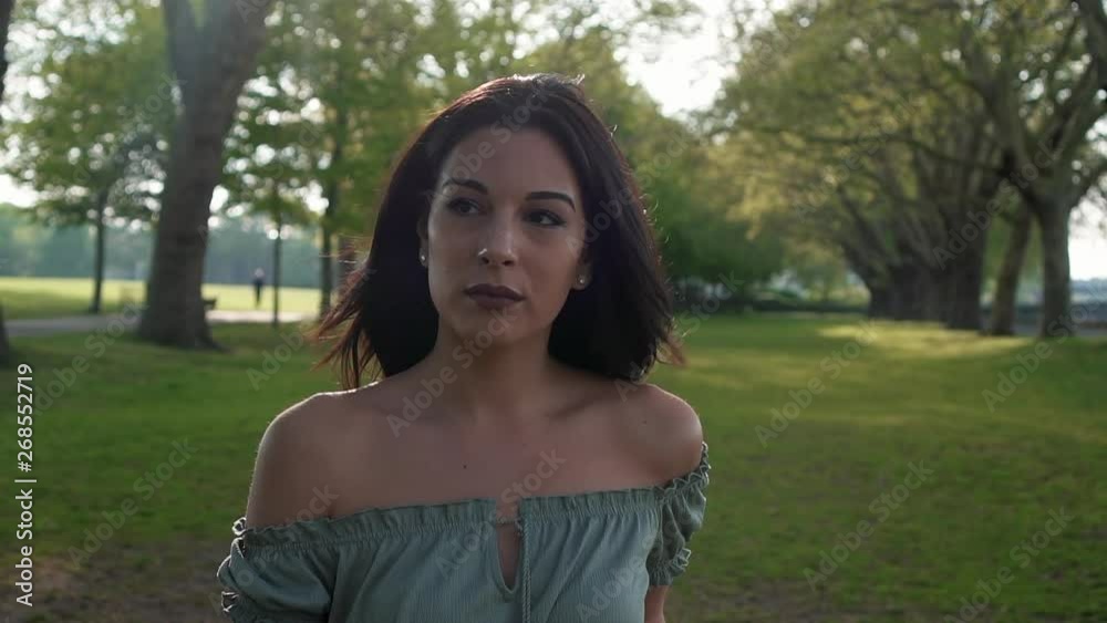 Slow Motion Portrait of a gorgeous hispanic latino young woman looking at the camera and show emotions from serious to smiling and laughing with a beautiful British park in the background. Slow Motion Portrait of a gorgeous hispanic latino young woman looking at the camera and show emotions from serious to smiling and laughing with a beautiful British park in the background.