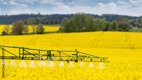 Agricultural sprayer detail. Flowering rapeseed field. Brassica napus. Working spraying machine in yellow canola land. Spring landscape. Chemical fertilizers, toxic pesticides, insecticides. Ecology.