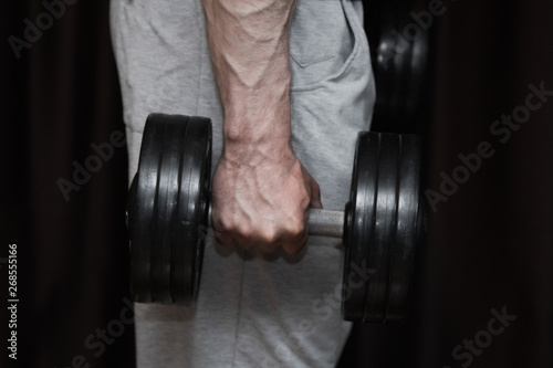 athlete trains biceps hands with dumbbells in the center of workouts on a black background. training tools in the gym close-up