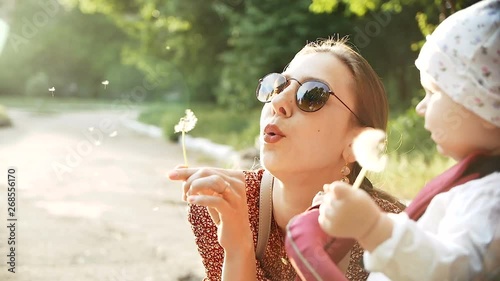 Mother and baby girl blowing on a dandelion flower in the summer in the park