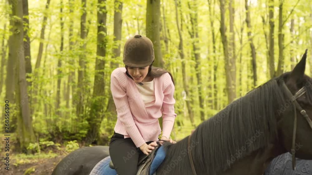 Young Beuatiful Caucasian Female Sitting in Saddle on Black Horse Preparing for Riding in Green Spring Forest. Light Camera Movement Young Beuatiful Caucasian Female Sitting in Saddle on Black Horse Preparing for Riding in Green Spring Forest. Light Camera Movement
