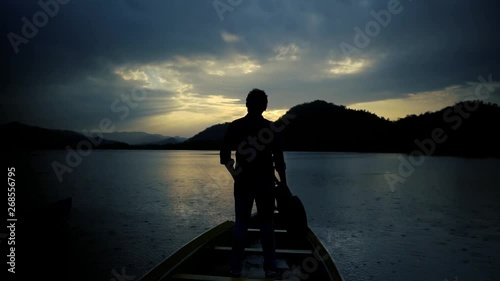 On a calmness lake, a lonely people with a guitar look round to the scenic landscape, from a wooden boat. photo