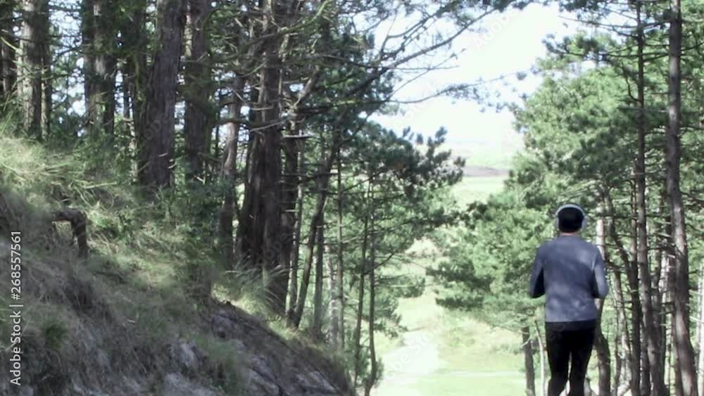Active man running in forest followed by another person walking. Shot from the back. Active man running in forest followed by another person walking. Shot from the back.