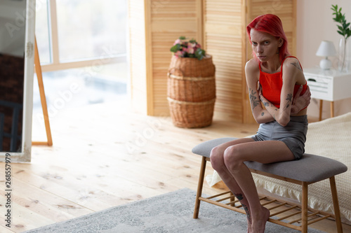 Red-haired anorexic woman sitting in bedroom near the window