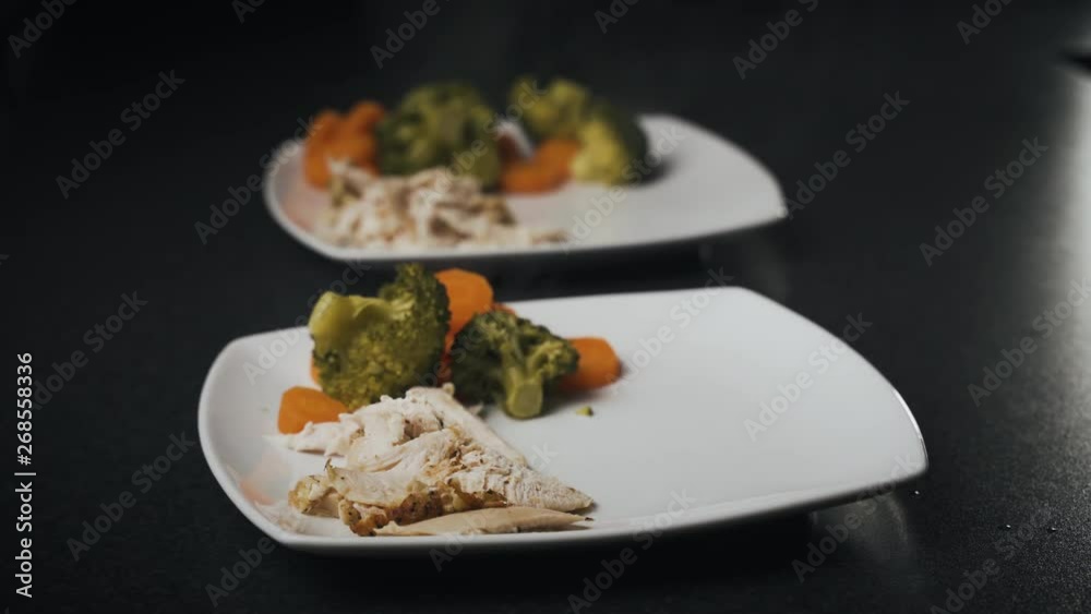 Steaming hot sliced carrots being added to white china dishes. Cooked broccoli and roast chicken on a white dish being prepared for a dinner meal. Steaming hot sliced carrots being added to white china dishes. Cooked broccoli and roast chicken on a white dish being prepared for a dinner meal.
