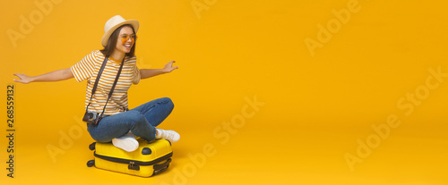 European Caucasian woman sitting on suitcase and spreading arms as if she is flying, concept of travelling, isolated