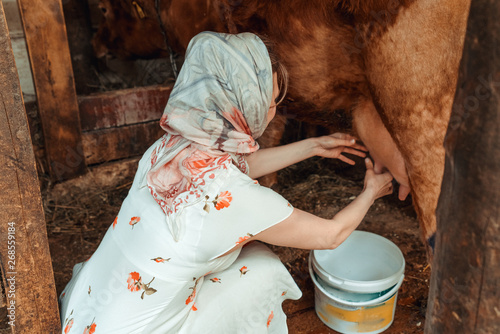 woman milkmaid milking a cow, farm photo
