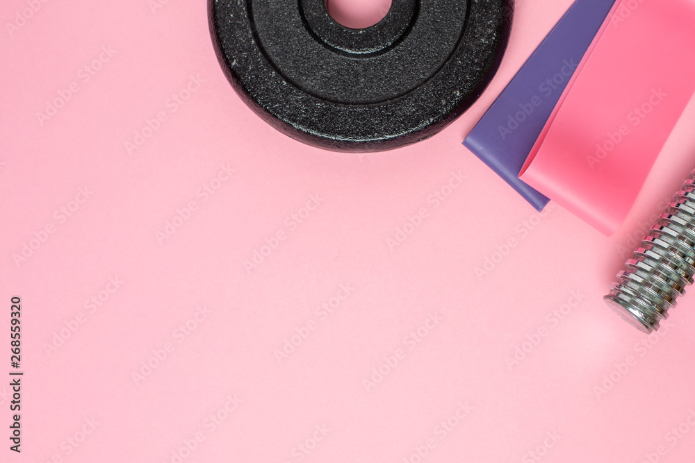 Fitness background.Athlete's set with dumbbells and elastic bands for stretching on a pastel pink background.
