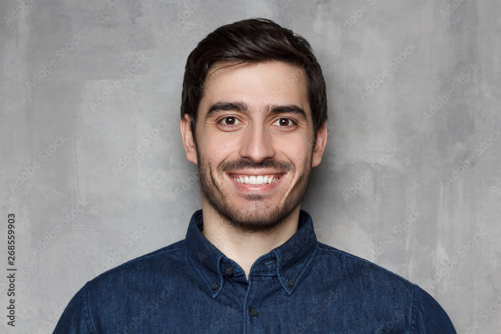 Headshot portrait of smiling young man isolated on gray wall background Headshot portrait of smiling young man isolated on gray wall background
