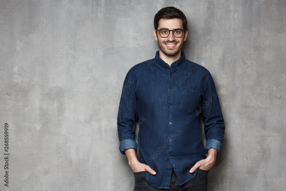Young handsome man wearing trendy glasses and denim shirt isolated on gray wall background with copy space