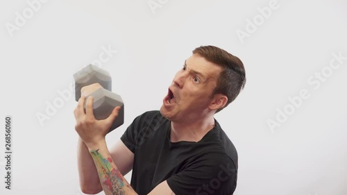 Funny man if exercising onver white background. Man athlete exercising dumbbell. Motivated athlete guy.  Use weights or dumbbells. A man showing his wimpy side and not wanting to work out.  photo