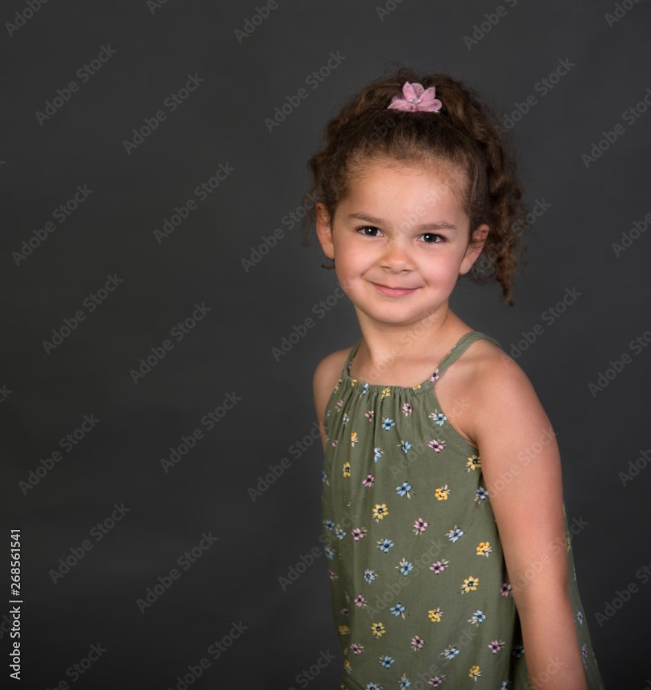 Beautiful smiling mixed race little girl with curly brown hair isolated on gray background Beautiful smiling mixed race little girl with curly brown hair isolated on gray background
