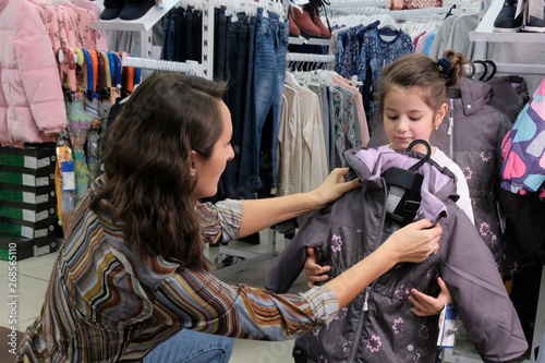 Young mother tries on children's clothes for autumn. Preparing for the winter season with a child. Buy a warm jacket for girls. Shopping with kids