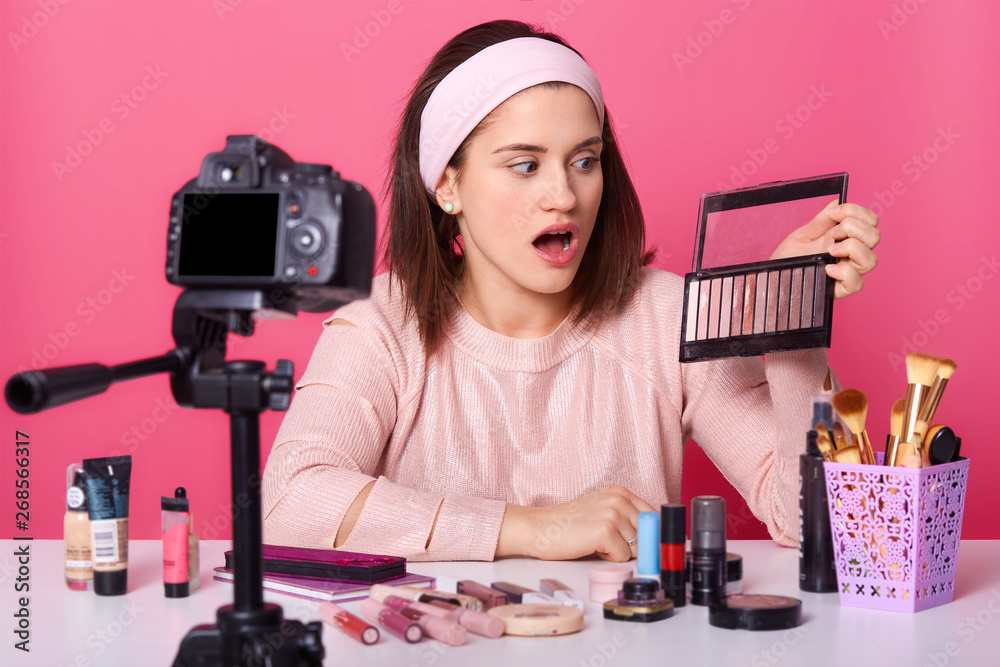 © sementsova321 - Surprised emotional lady looking at palette of colorful eyeshadow, holding it with one hand, opening mouth and eyes widely, sitting at table around other cosmetic products. Beauty bloggering concept. © sementsova321 - Surprised emotional lady looking at palette of colorful eyeshadow, holding it with one hand, opening mouth and eyes widely, sitting at table around other cosmetic products. Beauty bloggering concept.