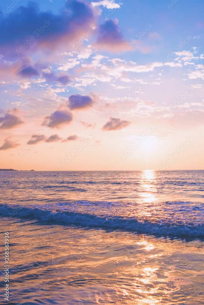 Pastel tropical beach sunset with waves and clouds in the blue sky