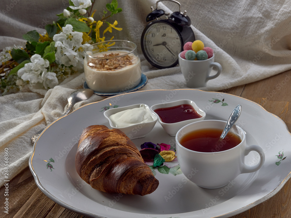 Croissant,jam ,tea with lemon, on a porcelain dish