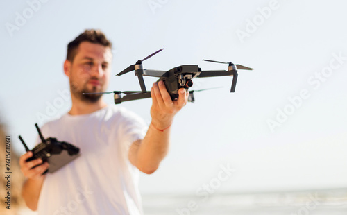 Young man holding drone before flight near ocean or sea. Pretty guy prepare to pilot outdoor
