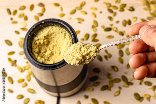 Pumpkin seeds in a coffee grinder. Pumpkin seeds powder in a spoon. Standing on a wooden table. Screensaver with space for text photo