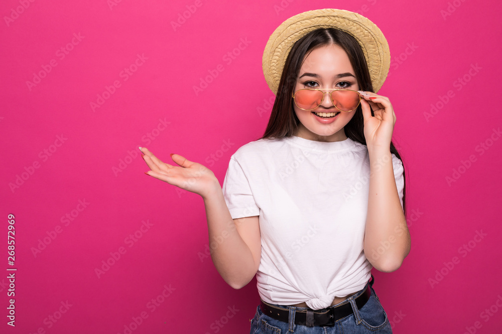 Asian pretty woman with open hand palm in sunglasses and straw hat isolated on pink background Asian pretty woman with open hand palm in sunglasses and straw hat isolated on pink background