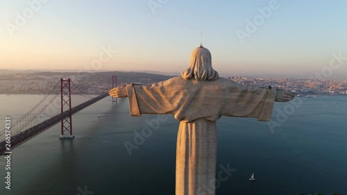 Aeria view monument Sanctuary of Christ the King. Drone flyby past near giant sculpture overlooking city of Lisbon Almada and famous 25th april bridge over river Tagus at sunset photo
