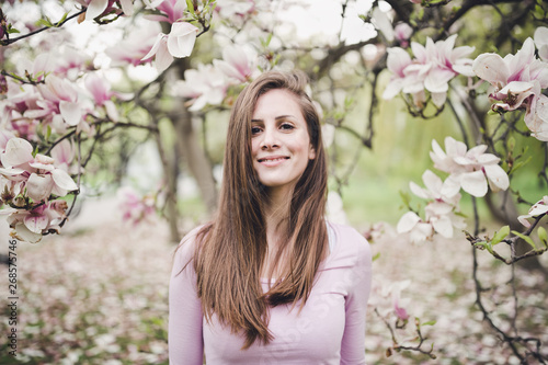 Cheerful long hair young woman under the blooming magnolia.