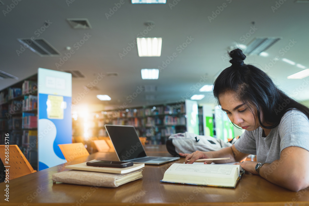 Asian female students learning and making notes writing down information in the library. Learning and preparing for university exam. Asian female students learning and making notes writing down information in the library. Learning and preparing for university exam.