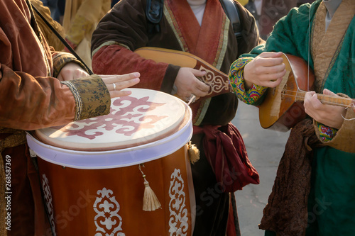 Street musicians in national costumes play folk instruments - a drum and a dombra during a holiday photo