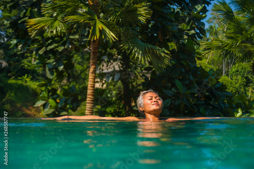 attractive and happy middle aged Asian woman relaxed at tropical resort infinity swimming pool with jungle background enjoying relaxed in luxury holidays trip © TheVisualsYouNeed