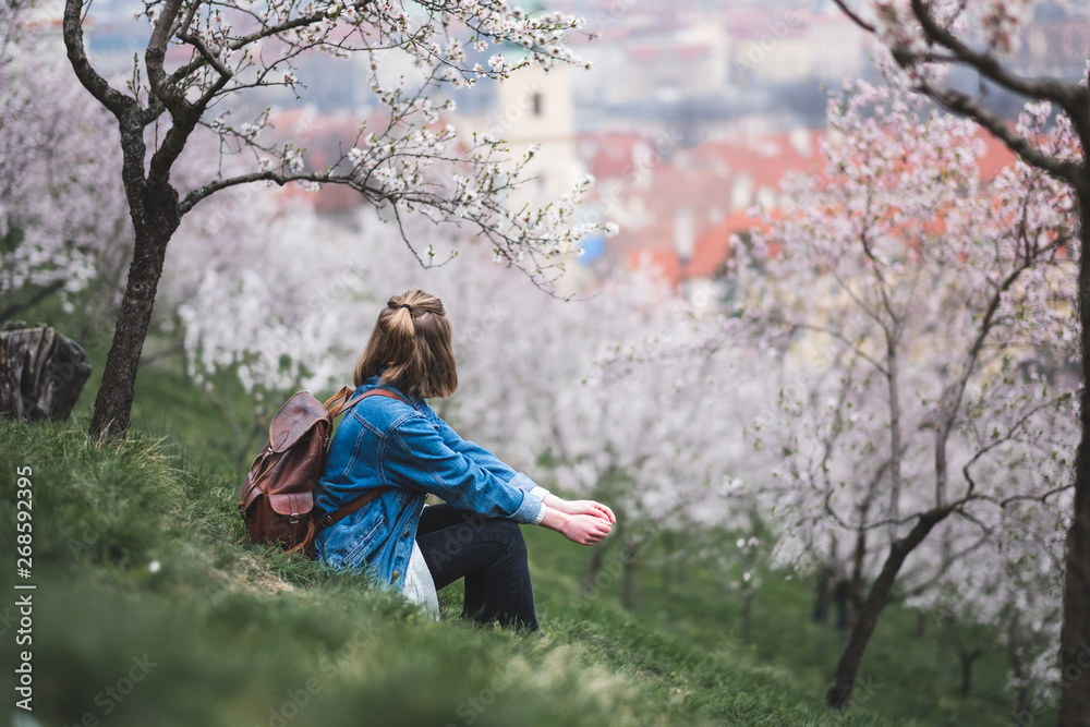 Woman sitting on green grass under blossoming trees on hill in center of Prague, Czech Republic Woman sitting on green grass under blossoming trees on hill in center of Prague, Czech Republic