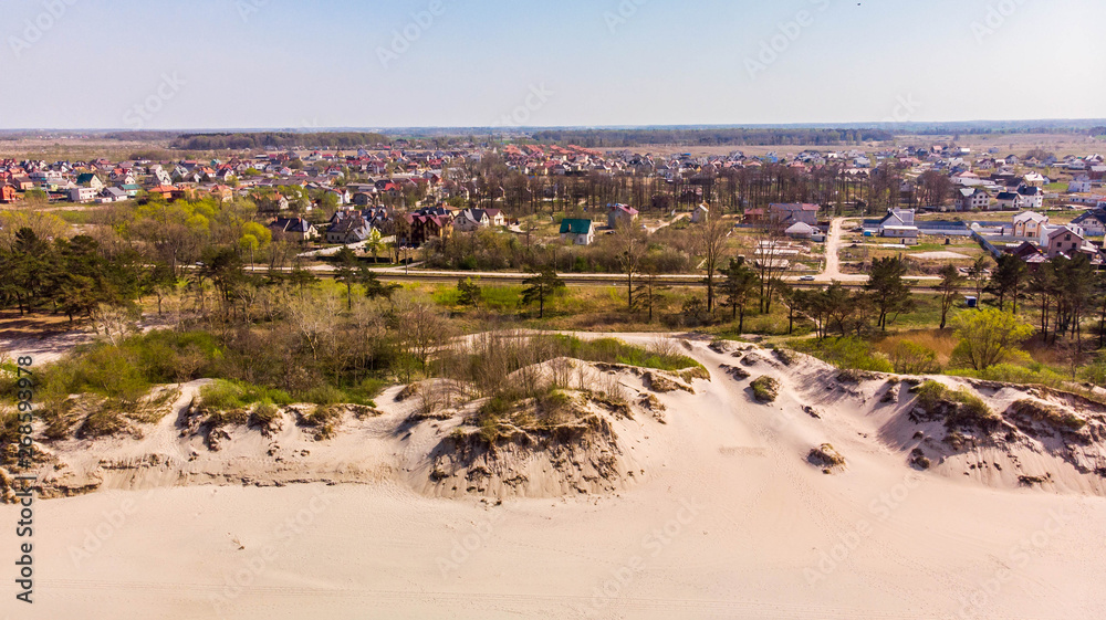 Fototapeta premium Amazing aerial view of the village with a lot of greenery, next to the sand dunes on a bright sunny day