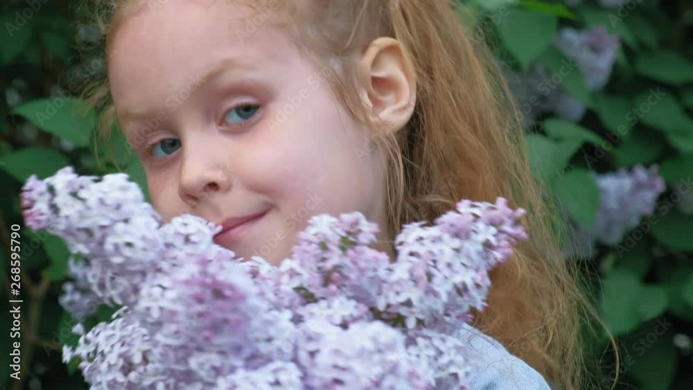 A little girl outdoors in a park or garden holds lilac flowers. Lilac bushes in the background. Summer, park A little girl outdoors in a park or garden holds lilac flowers. Lilac bushes in the background. Summer, park