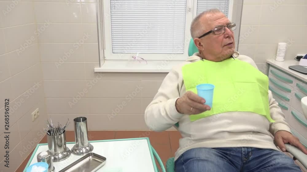 elderly man in glasses and with yellow napkin on chest rinses mouth with water and spits close view elderly man in glasses and with yellow napkin on chest rinses mouth with water and spits close view