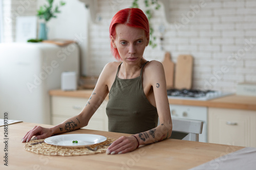 Anorexic woman having awful look sitting in the kitchen