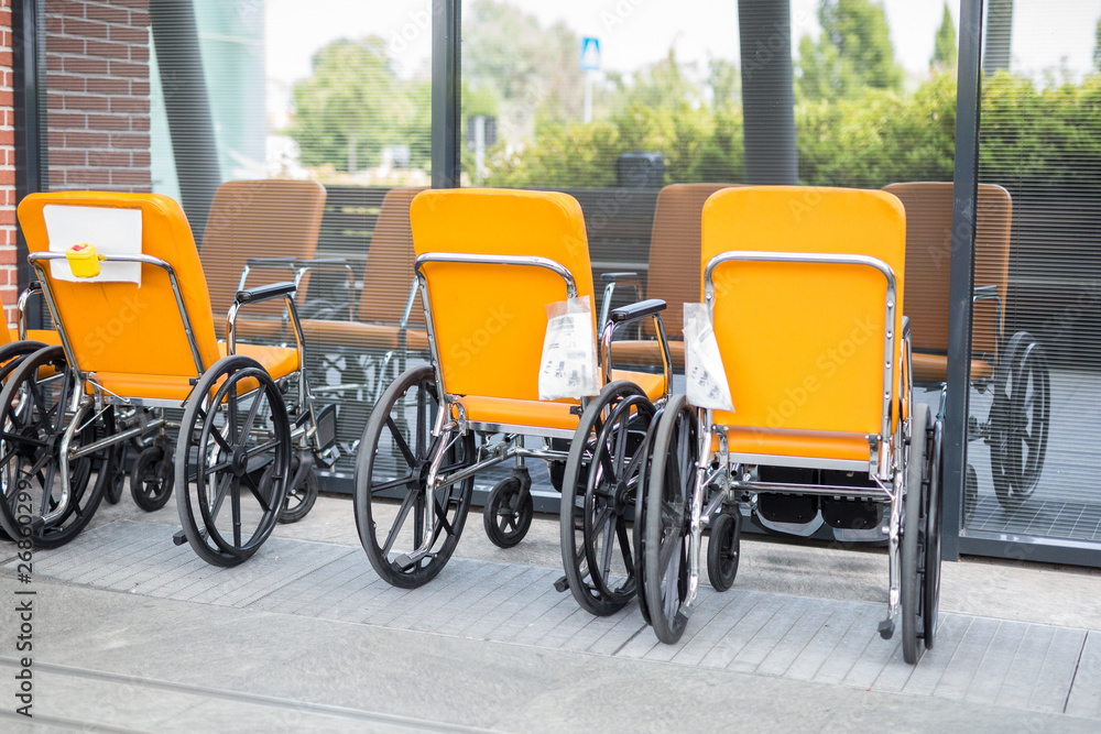 Group of Empty and Orange Color Wheelchairs in front of a Hospital Window