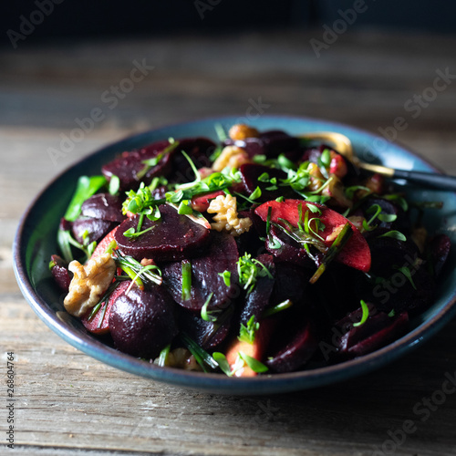Roasted beet/beetroot, apples, walnuts, microgreens, winter salad, scallions salad in a blue pottery bowl with homemade vinaigrette and golden spoon on rustic wooden table. 